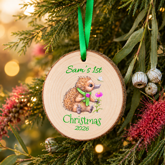 Personalised Echidna First Christmas 2026 wood slice ornament with green ribbon hanging among Australian native foliage